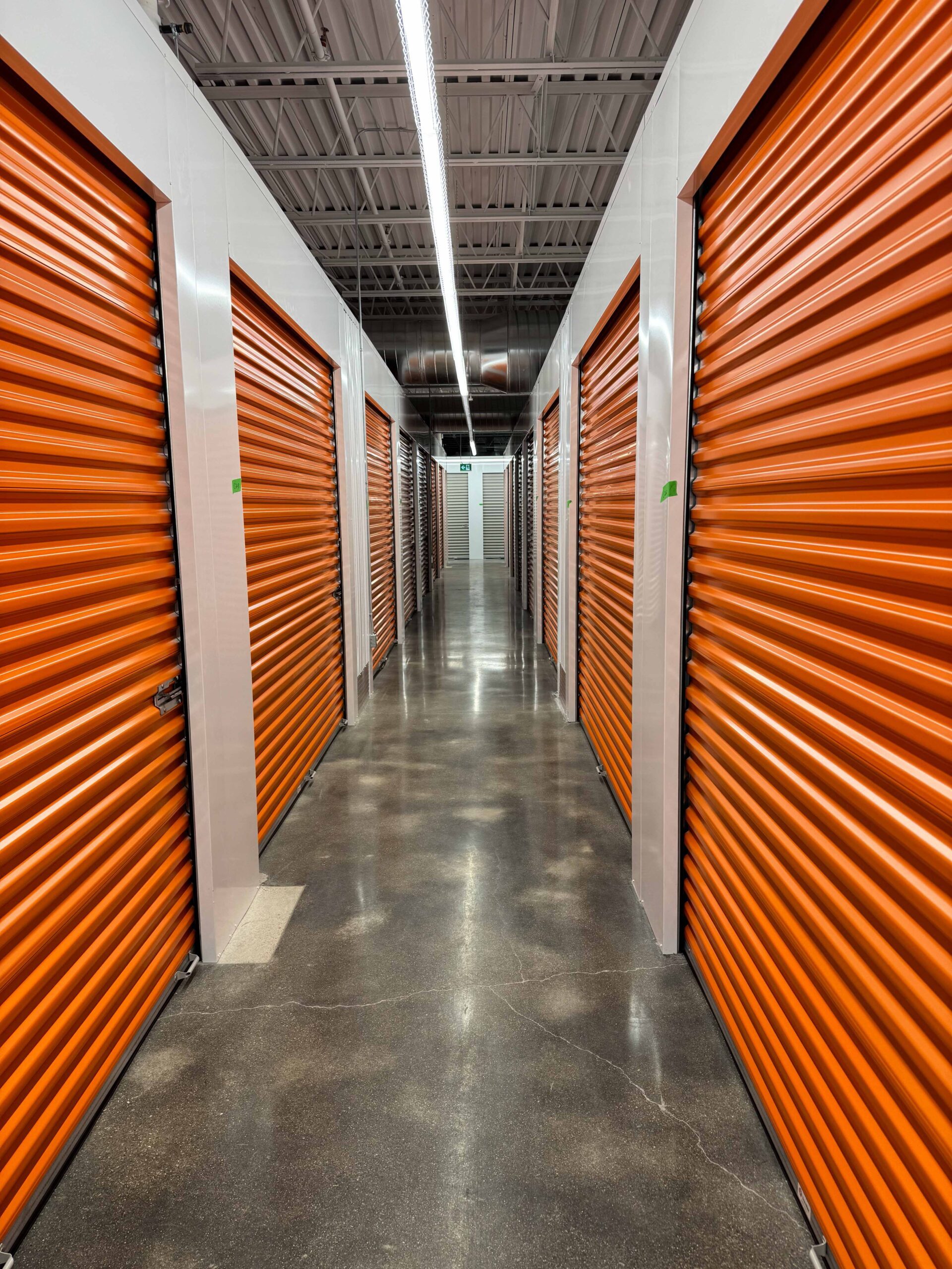 Self-storage corridor with orange roll-up unit doors installed by NeoTech Construction