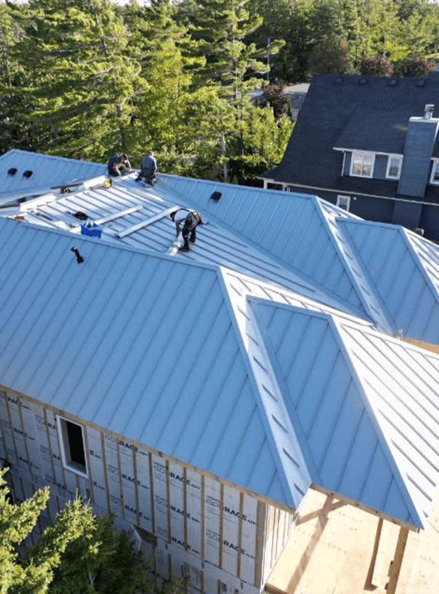 Installers fitting a blue standing seam metal roof on a commercial building